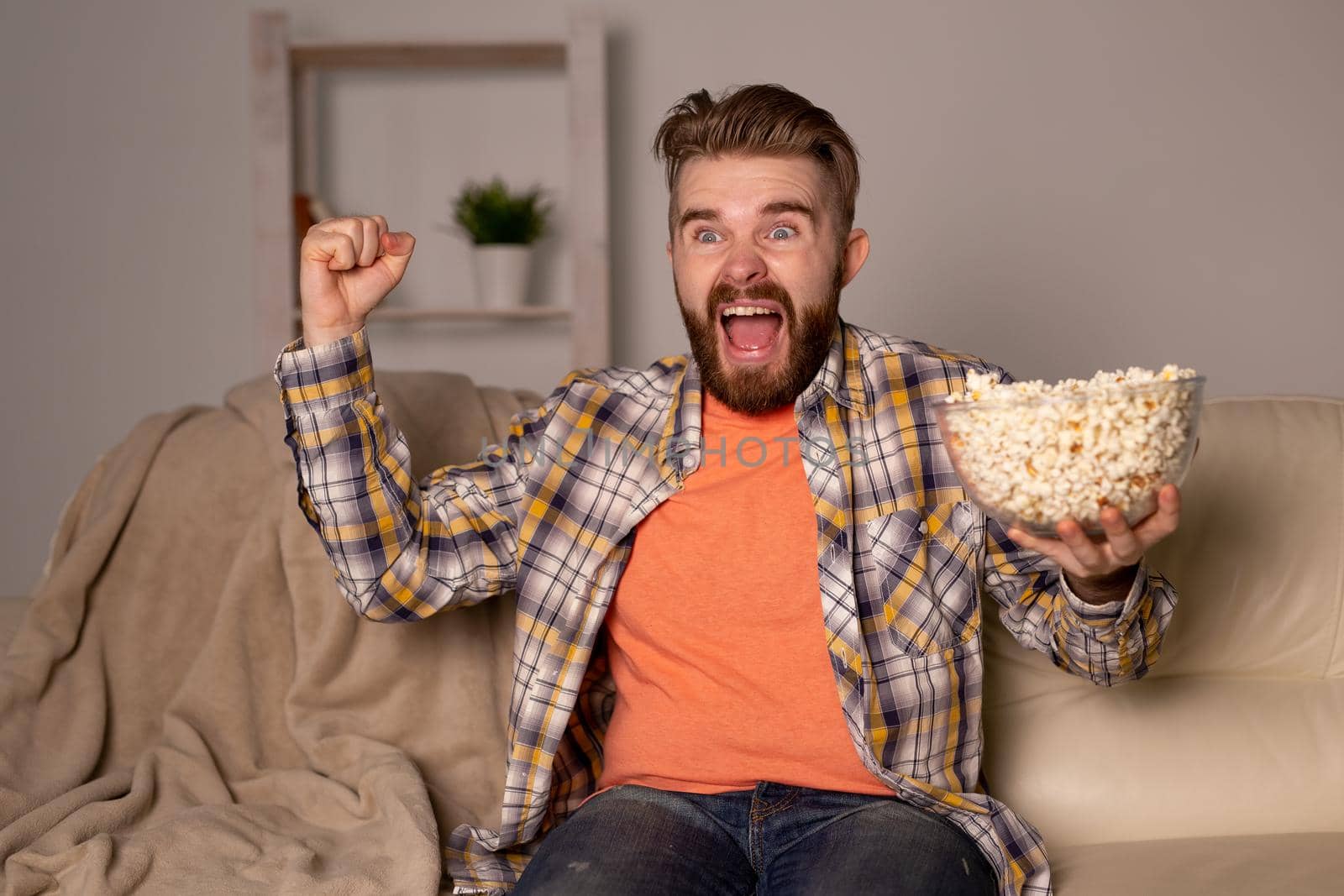 Bearded man watching film or sport games TV eating popcorn in house at night. Cinema, championship and fan.