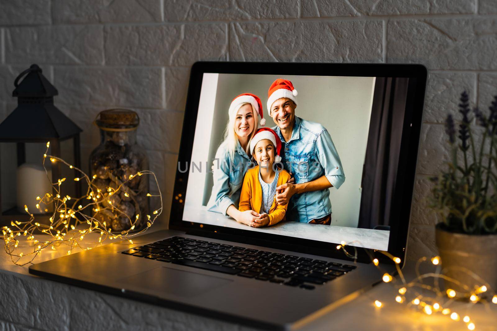 Happy parents hugging cute small kid daughter holding present giving Christmas gift to web camera during virtual family social meeting on video conference call party at home, laptop webcam view. by Andelov13