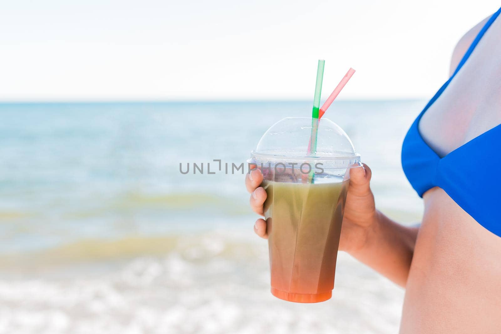 A young girl teenager holds and drink a colored cold non-alcoholic cocktail in her hand against the background of the sea beach by AYDO8