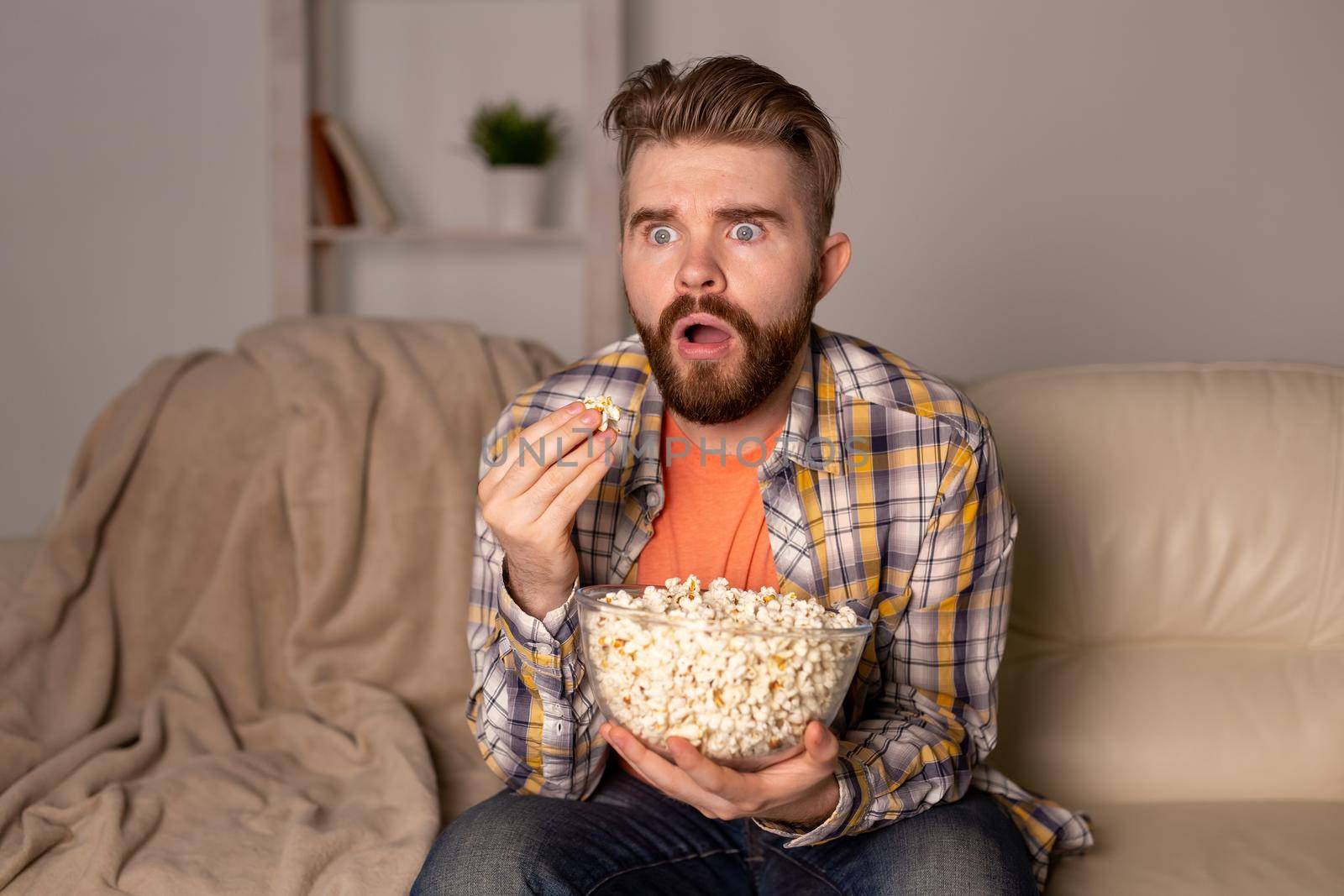 Bearded man watching film or sport games TV eating popcorn in house at night. Cinema, championship and fan.
