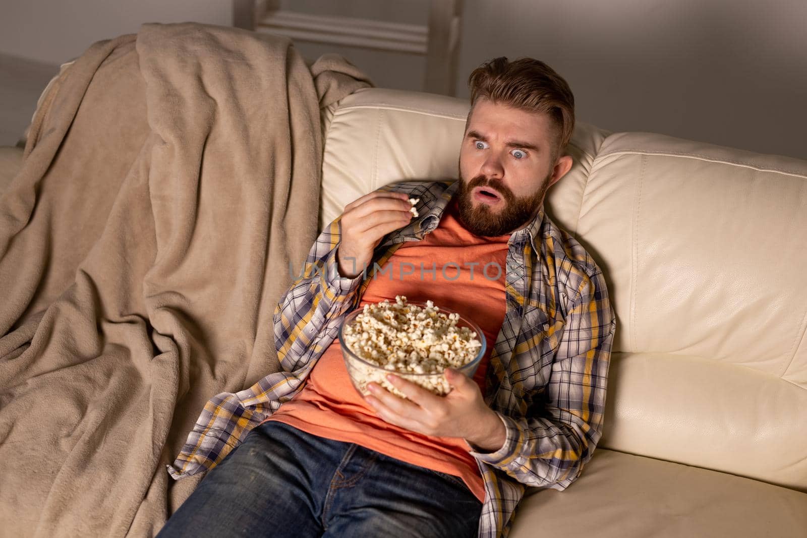 Bearded man watching film or sport games TV eating popcorn in house at night. Cinema, championship and fan.