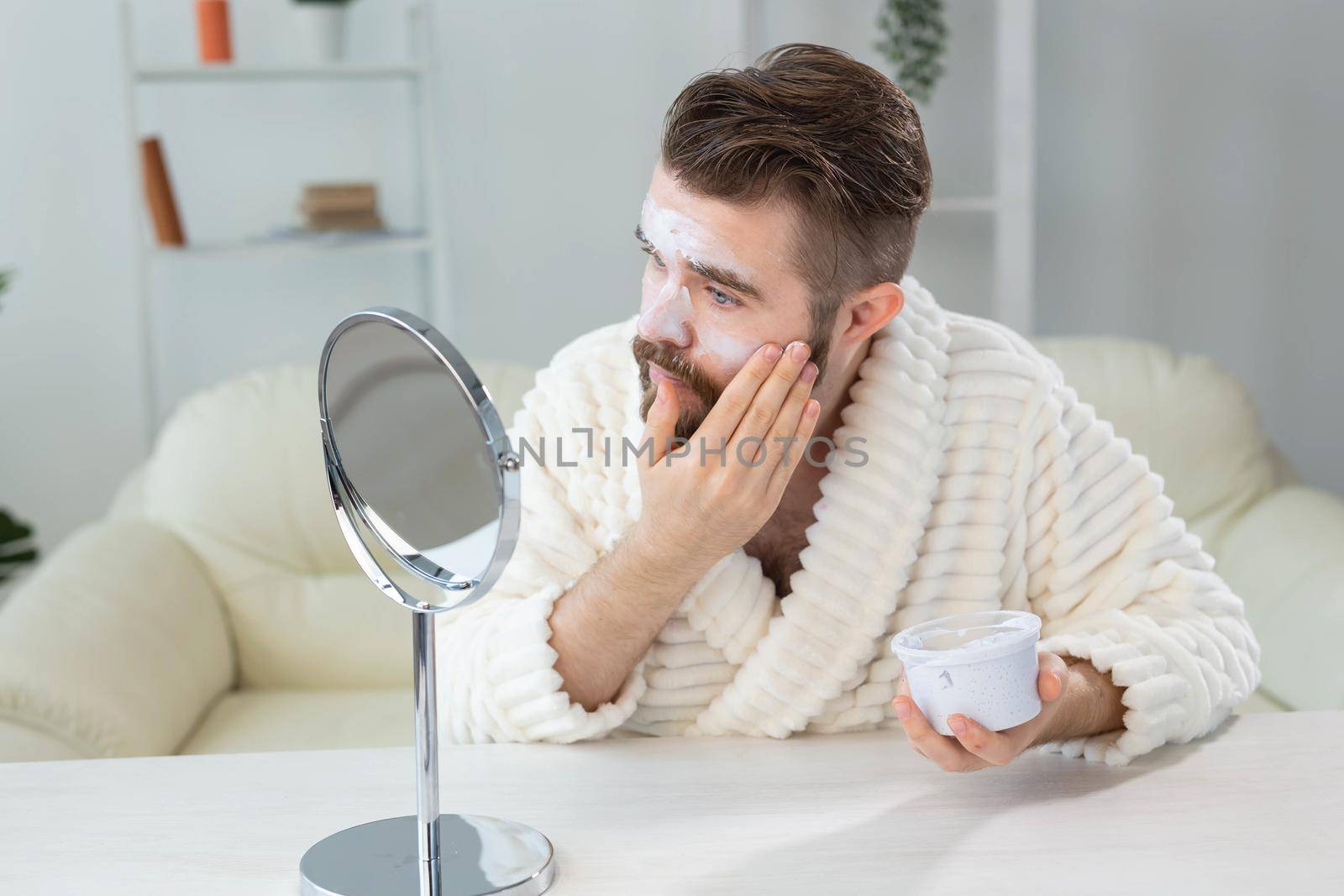 Bearded guy applying anti-wrinkle cream on his face. Skin care and spa for man concept