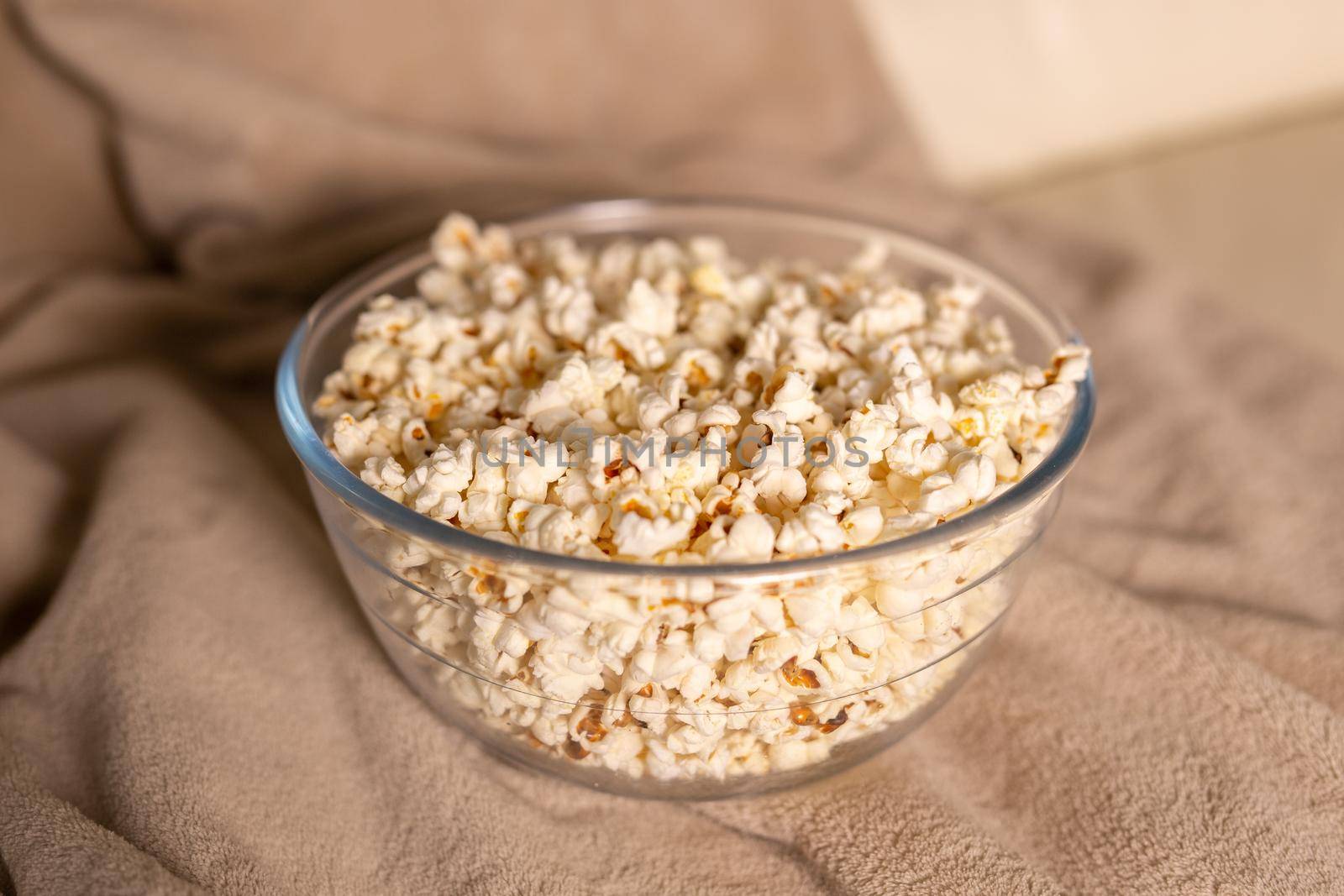 Bowl of popcorn for watching a film on a beige couch. Snacks and unhealthy junk food.