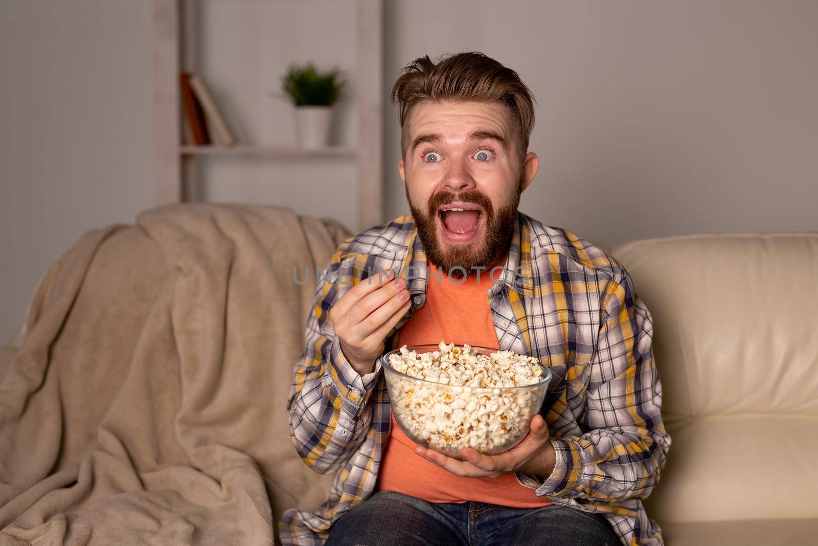 Bearded man watching film or sport games TV eating popcorn in house at night. Cinema, championship and fan.
