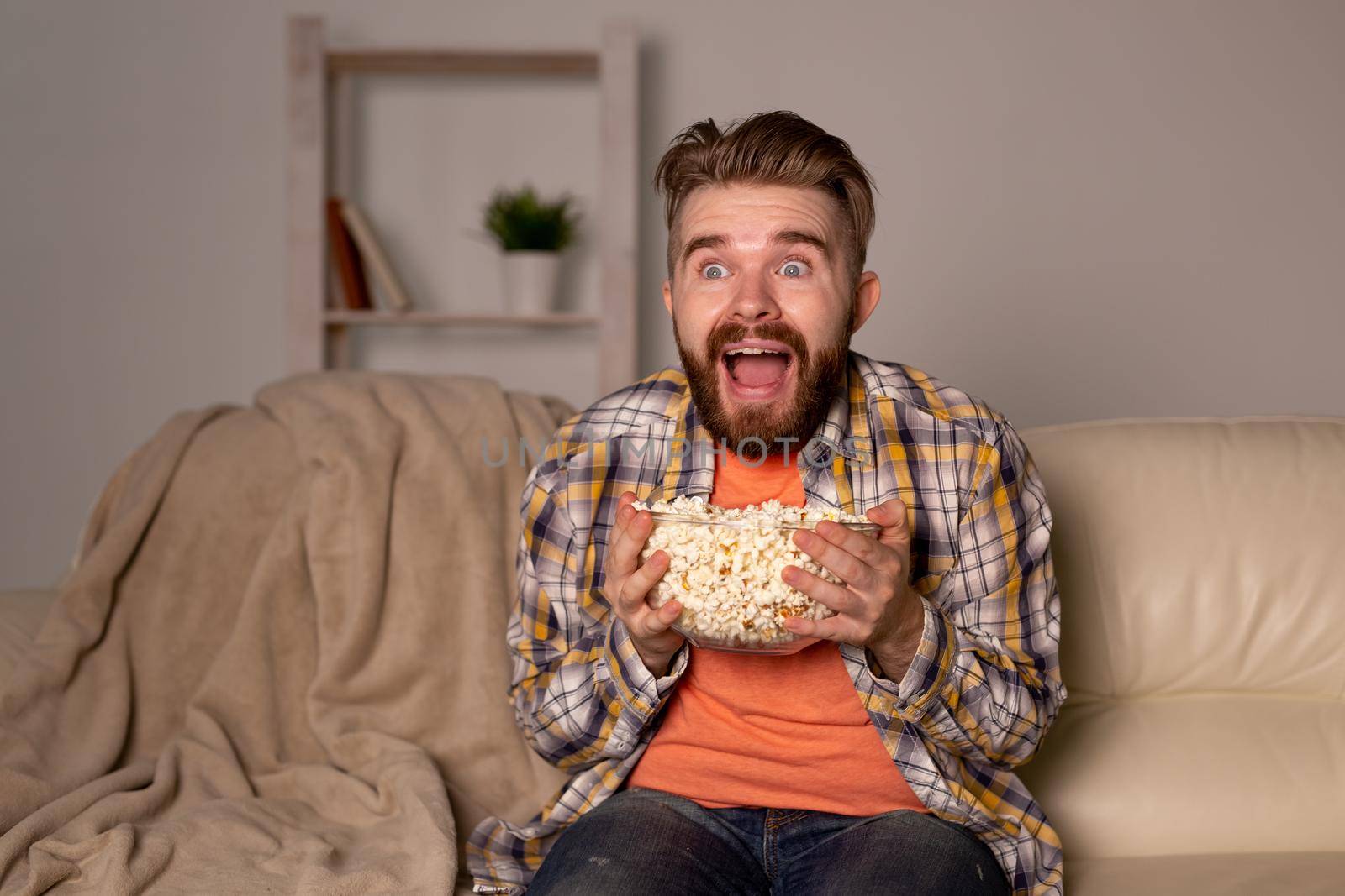 Bearded man watching film or sport games TV eating popcorn in house at night. Cinema, championship and fan.