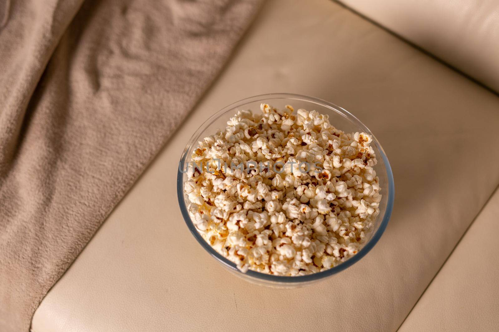 Bowl of popcorn for watching a film on a beige couch. Snacks and unhealthy junk food.