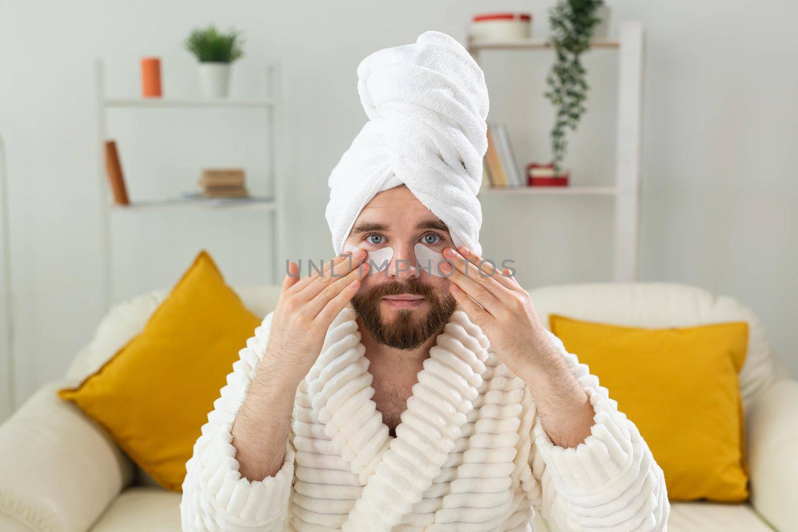 Young man with patches under the eyes at home. Concept of cosmetology for men.Spa at home, body and skin care.