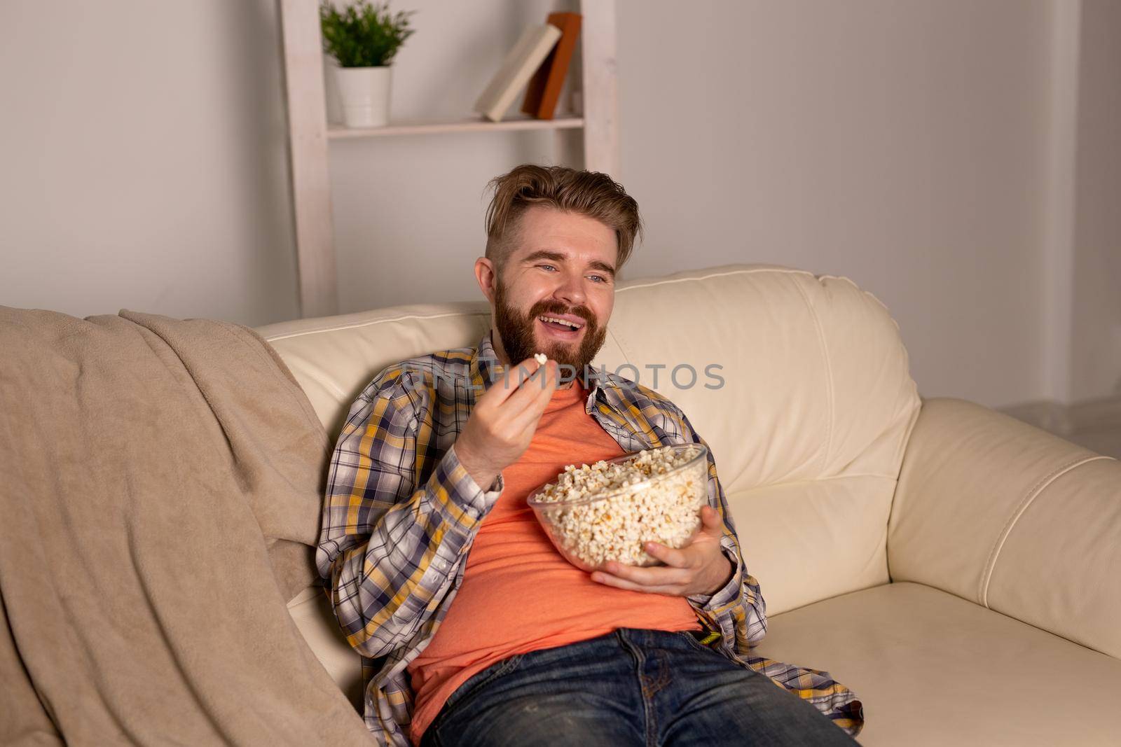 Bearded man watching film or sport games TV eating popcorn in house at night. Cinema, championship and fan.