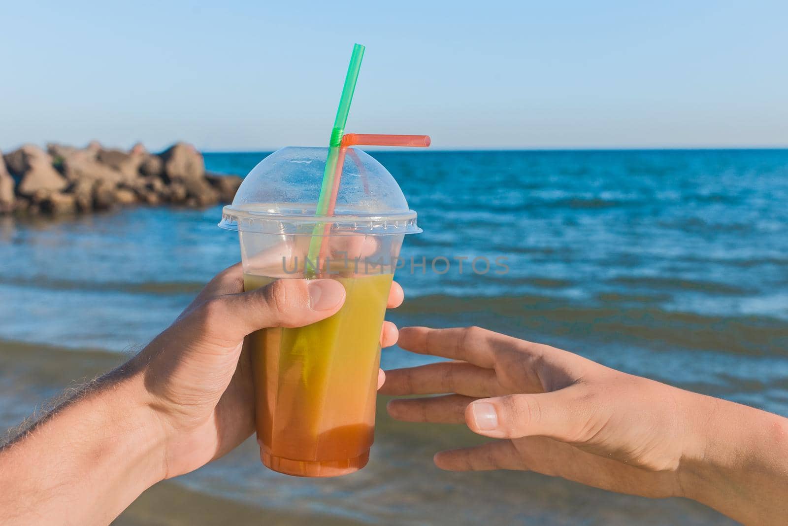 The guy's hand passes a colored chilled non-alcoholic cocktail into the girl's hand against the background of sea water.
