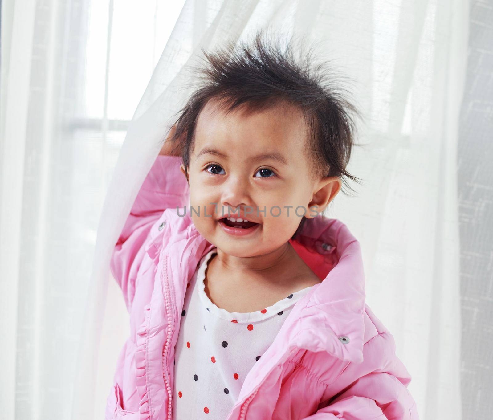 baby playing hide and seek behind the curtain at home