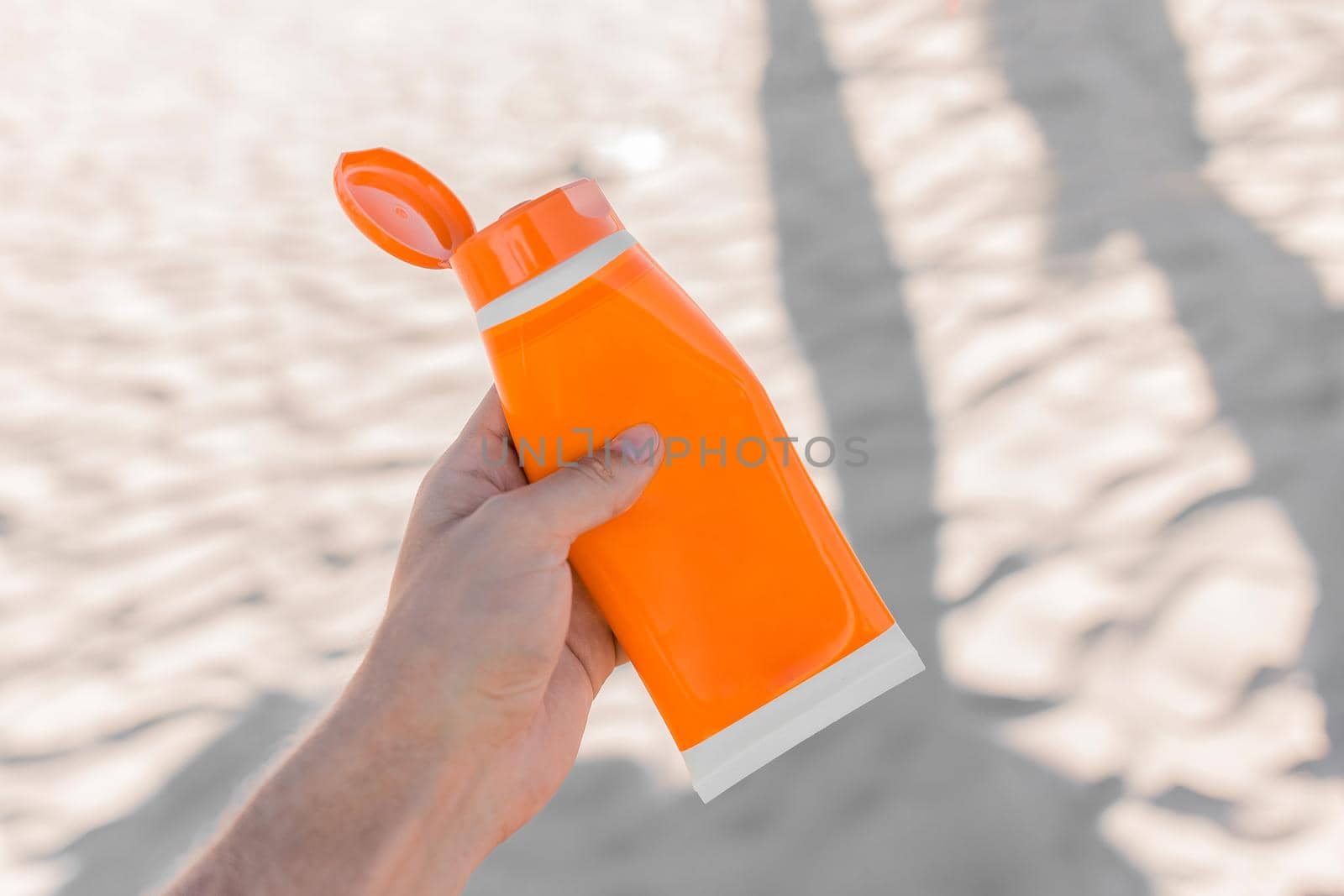 The guy's hand holds sunscreen against the background of the beach.