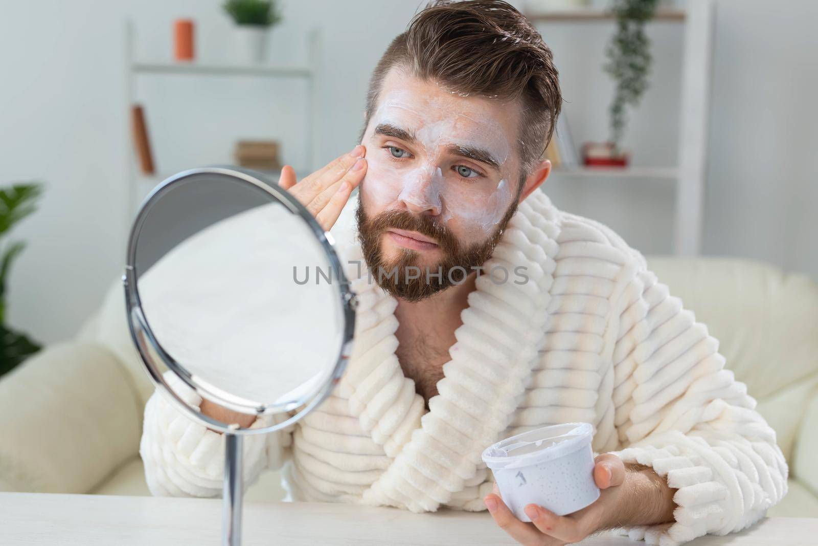 Bearded guy applying anti-wrinkle cream on his face. Skin care and spa for man concept