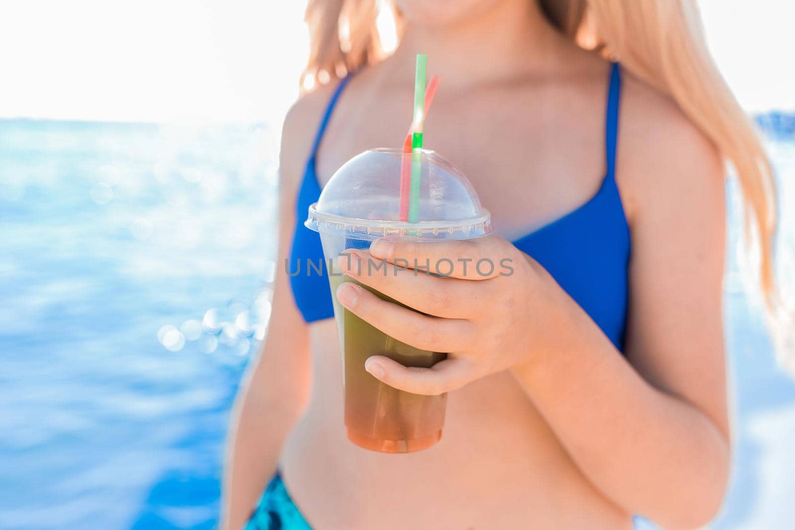 A young girl teenager holds and drink a colored cold non-alcoholic cocktail in her hand against the background of the sea beach.