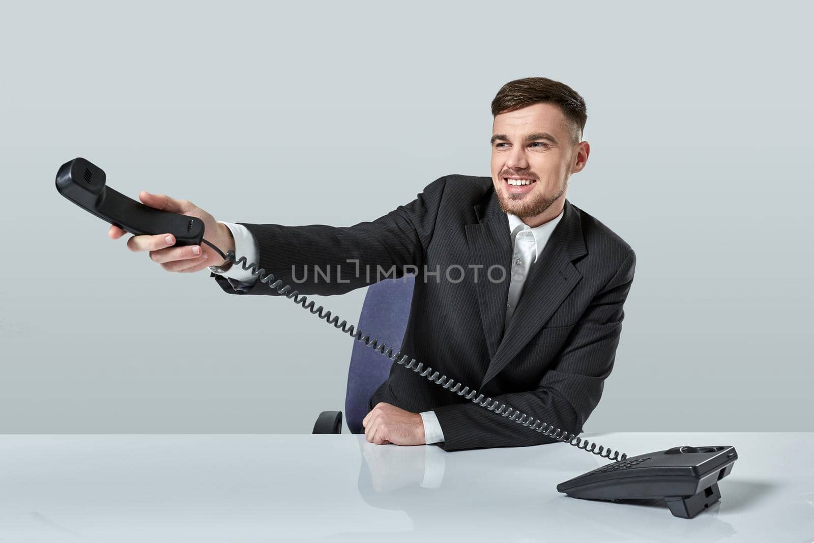 Portrait of attractive businessman holding telephone in his hand. This call is for you concept. A young man in a black suit dials the phone number while sitting in the office