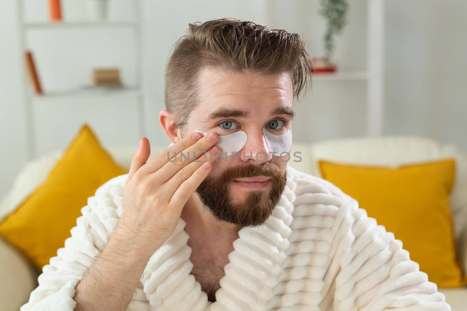 Bearded man applying eye patches on his face. Wrinkles and face home care for men
