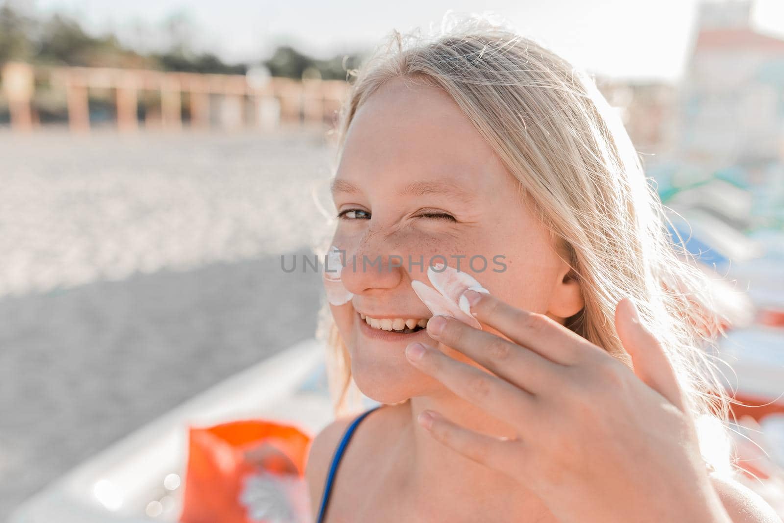 Close-up portrait of a young sweet and happy teenage girl smearing sunscreen on her face.