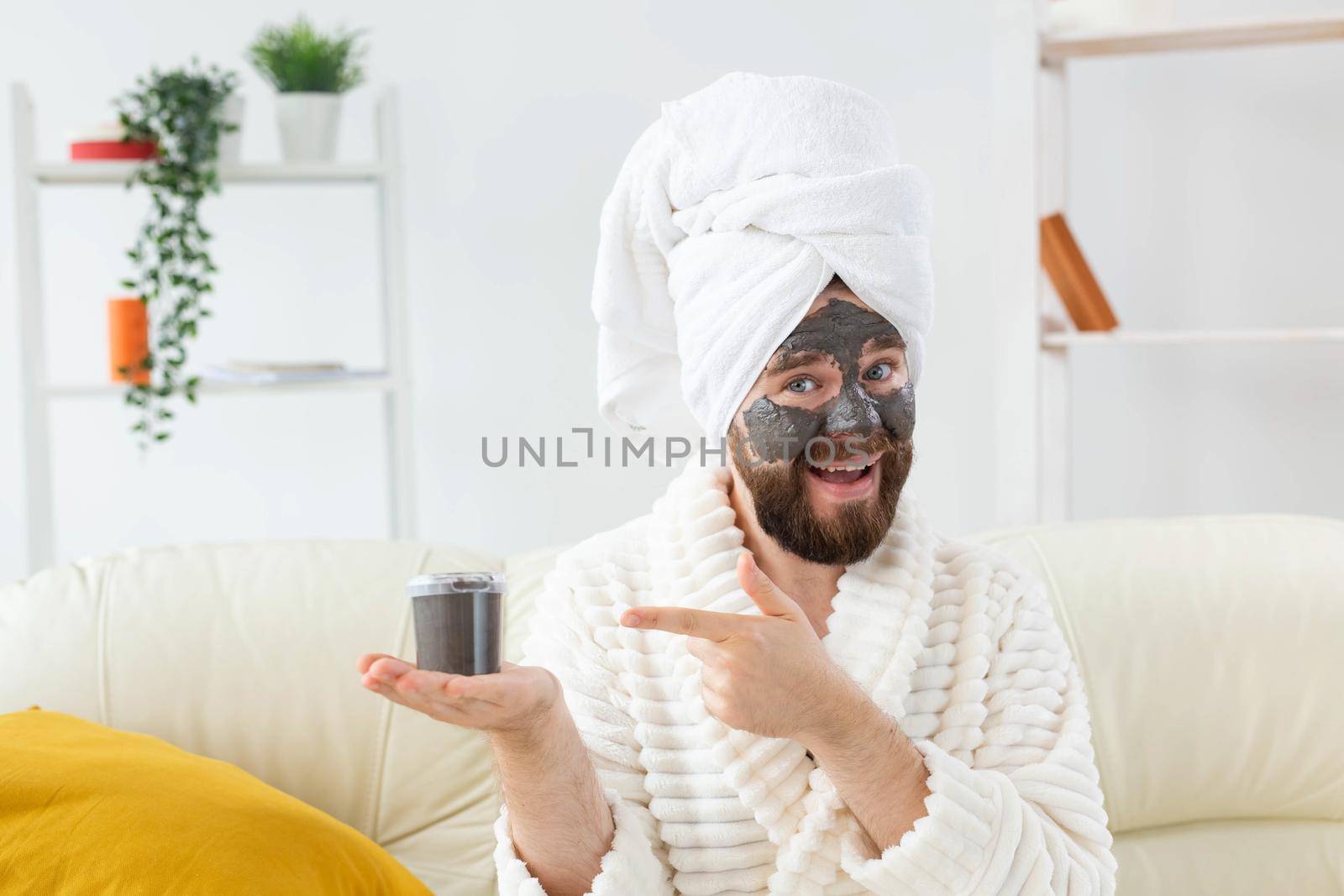 Bearded man having fun with a cosmetic mask on his face made from black clay. Men skin care and spa at home.