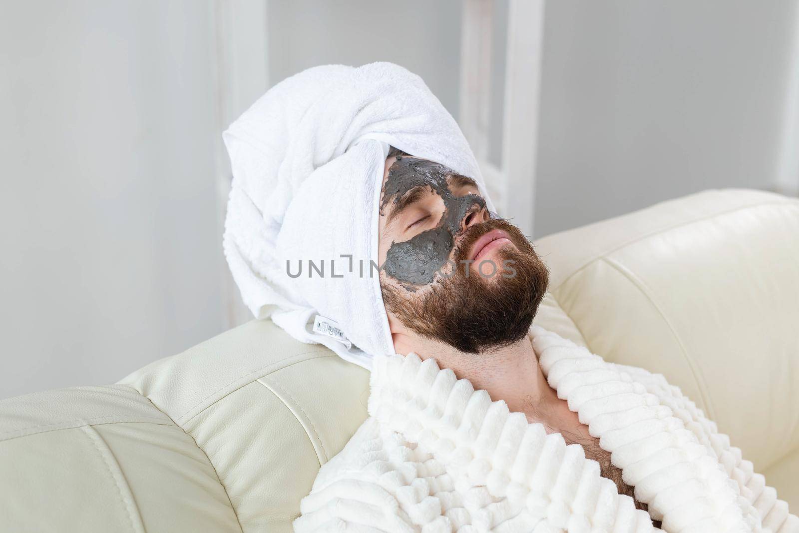 Bearded man has clean fresh skin, wears beauty clay mask on face and enjoys beauty treatments. Spa at home, body and skin care.