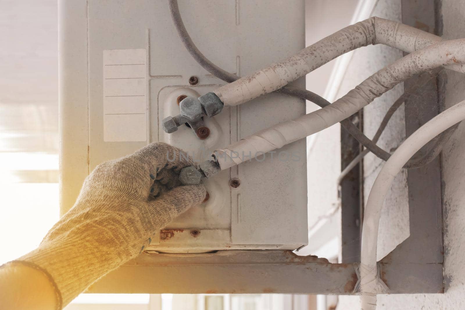 The hand of an air conditioner repair and maintenance specialist in a construction glove working with air-conditioned old equipment.