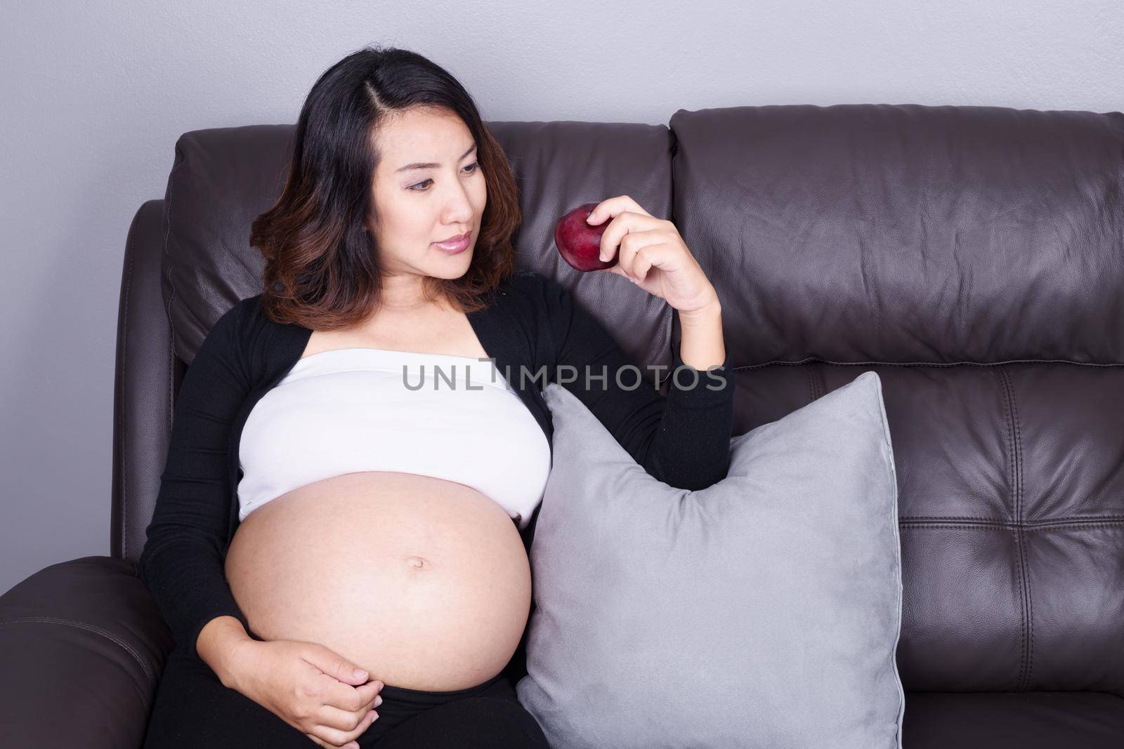 portrait of pregnant woman resting with red apple at home on sofa