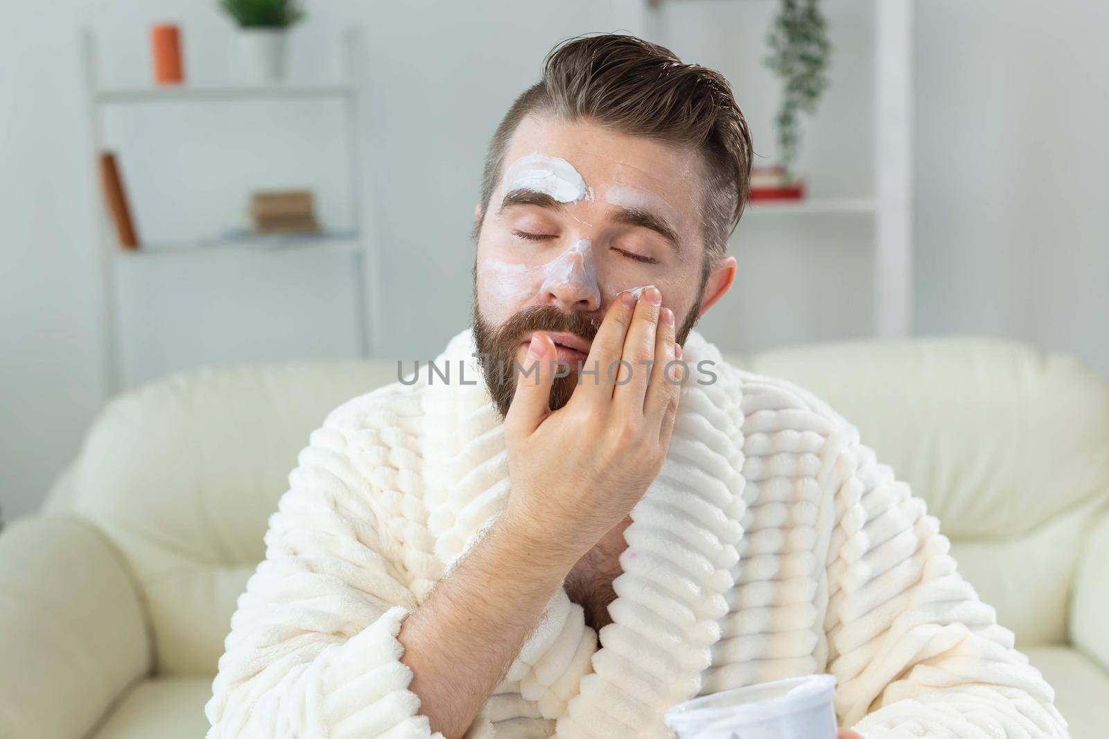 Closeup of handsome young man applying facial cream in front of mirror