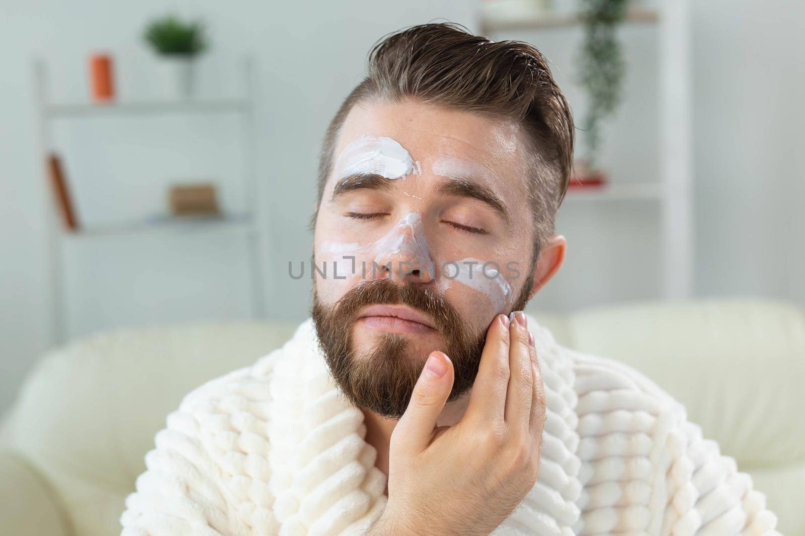 Bearded guy applying anti-wrinkle cream on his face. Skin care and spa for man concept