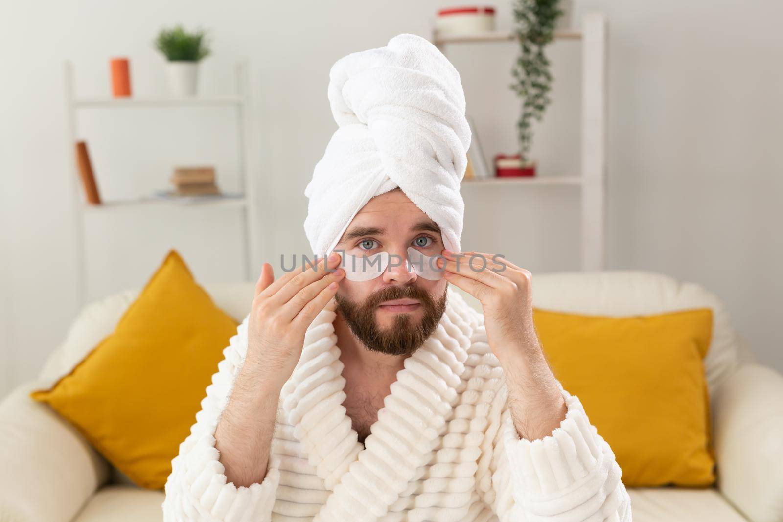 Bearded man applying eye patches on his face. Wrinkles and face home care for men