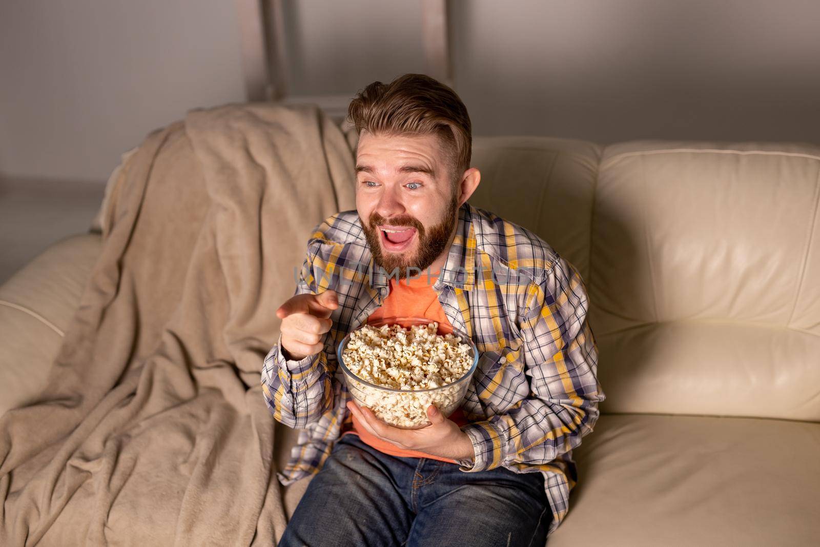 Bearded man watching film or sport games TV eating popcorn in house at night. Cinema, championship and fan.