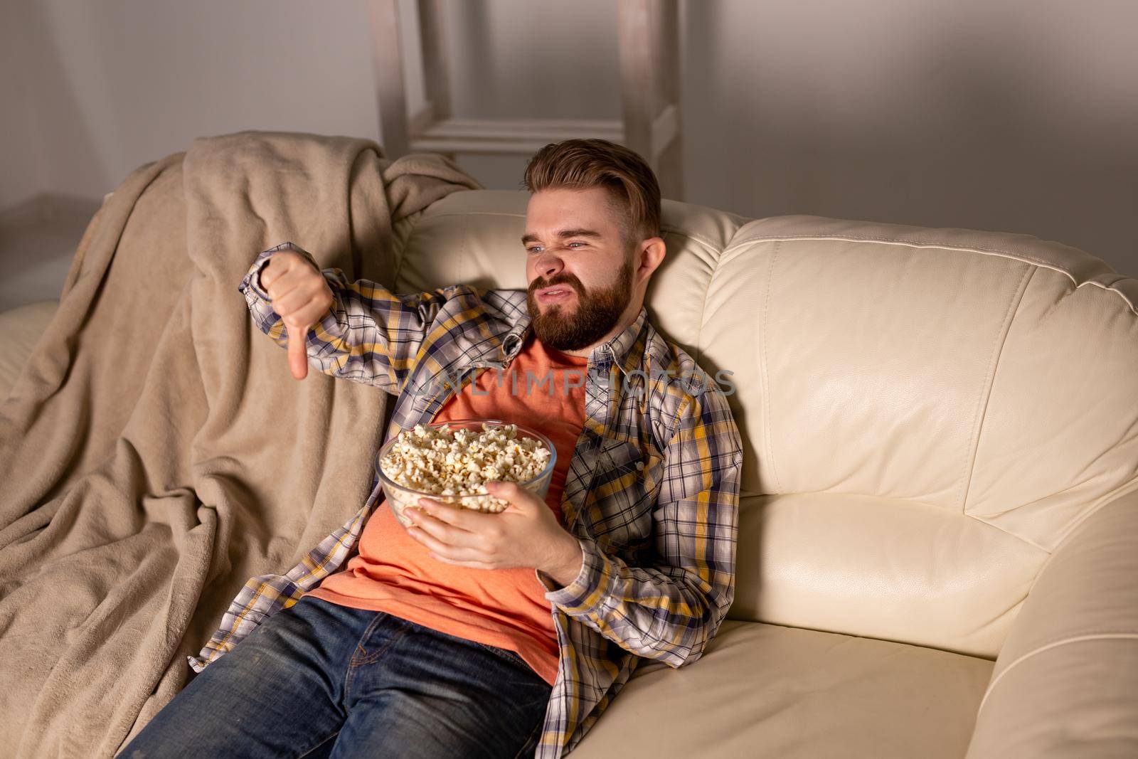 Bearded man watching film or sport games TV eating popcorn in house at night. Cinema, championship and fan.