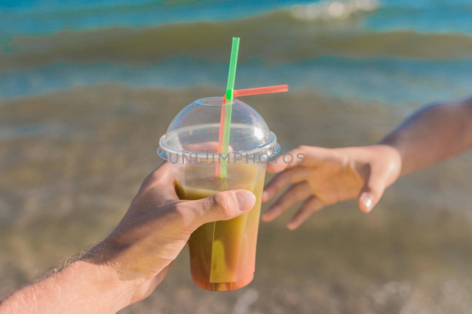 The guy's hand passes a colored chilled non-alcoholic cocktail into the girl's hand against the background of sea water.