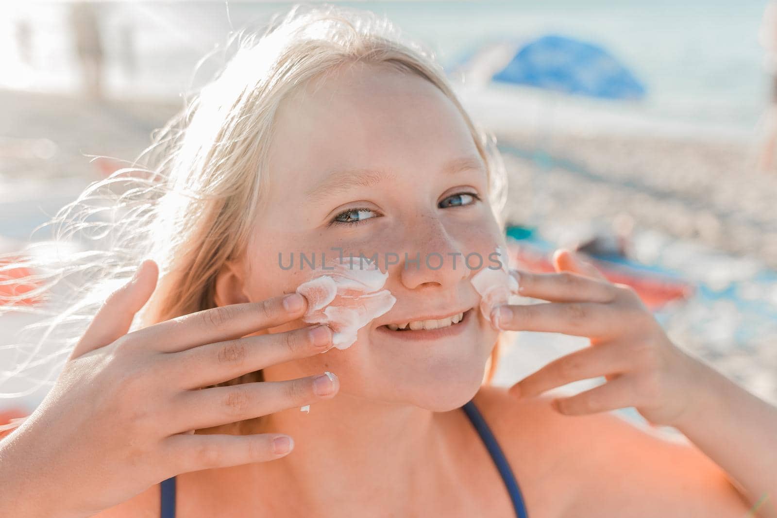 Close-up portrait of a young sweet and happy teenage girl smearing sunscreen on her face.