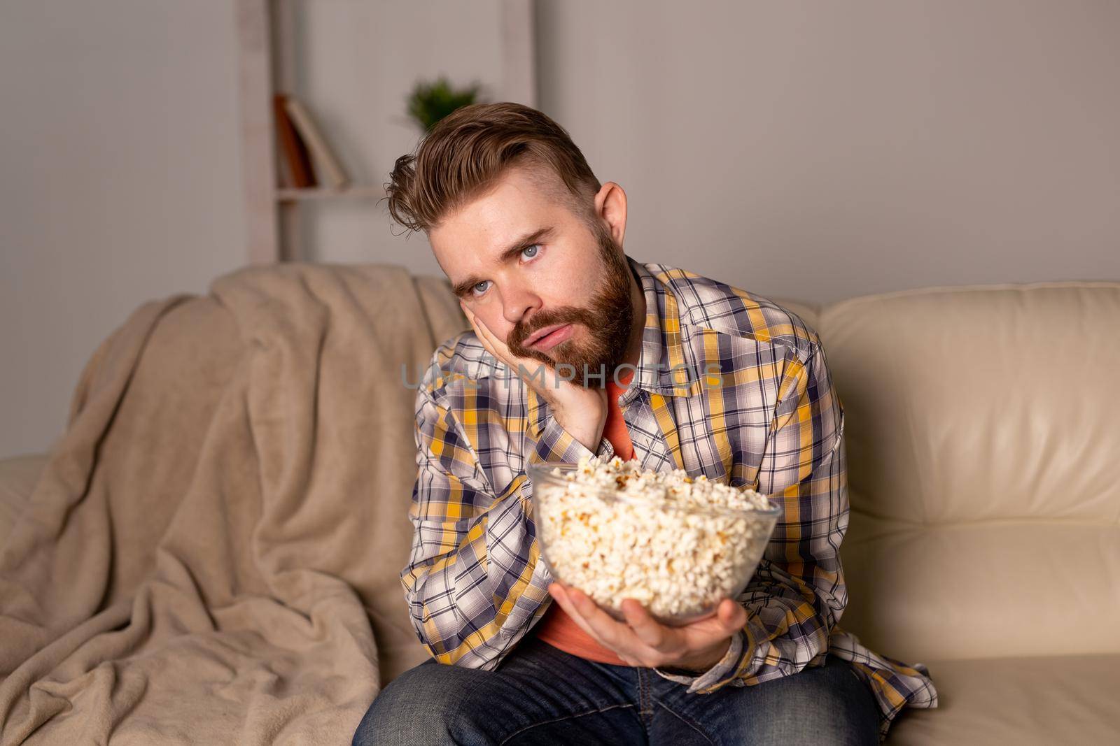 Bearded man watching film or sport games TV eating popcorn in house at night. Cinema, championship and fan.