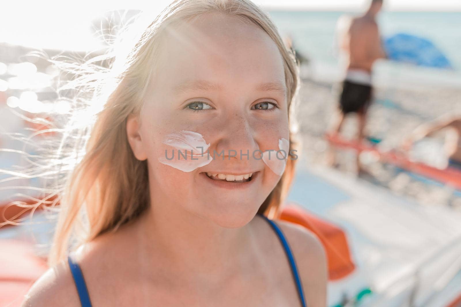 Close-up portrait of the face of a young positive attractive girl with sunscreen and sun protection on her cheeks by AYDO8