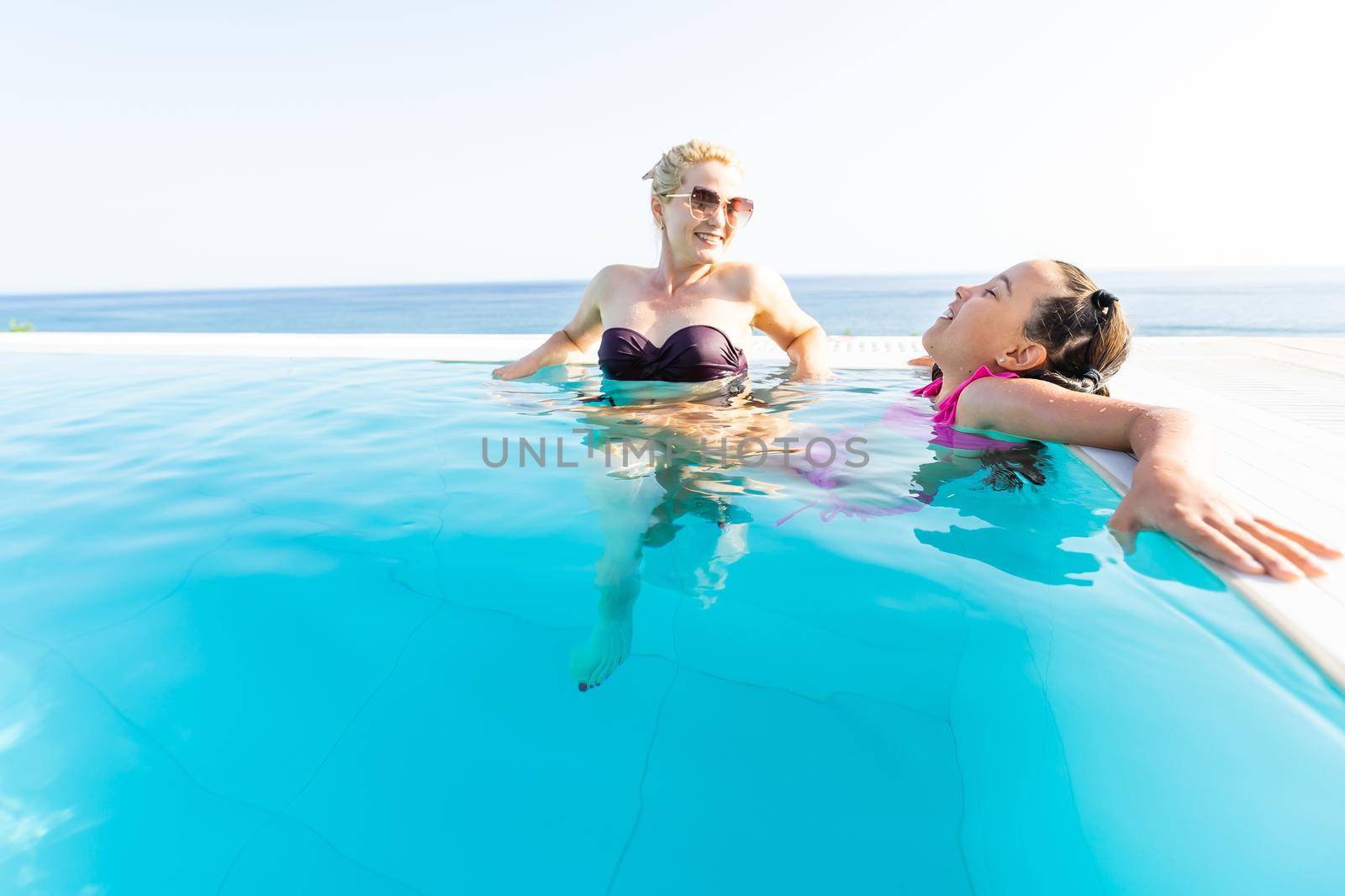 Smiling beautiful woman smears with cream for sunburn little girl near pool in aquapark