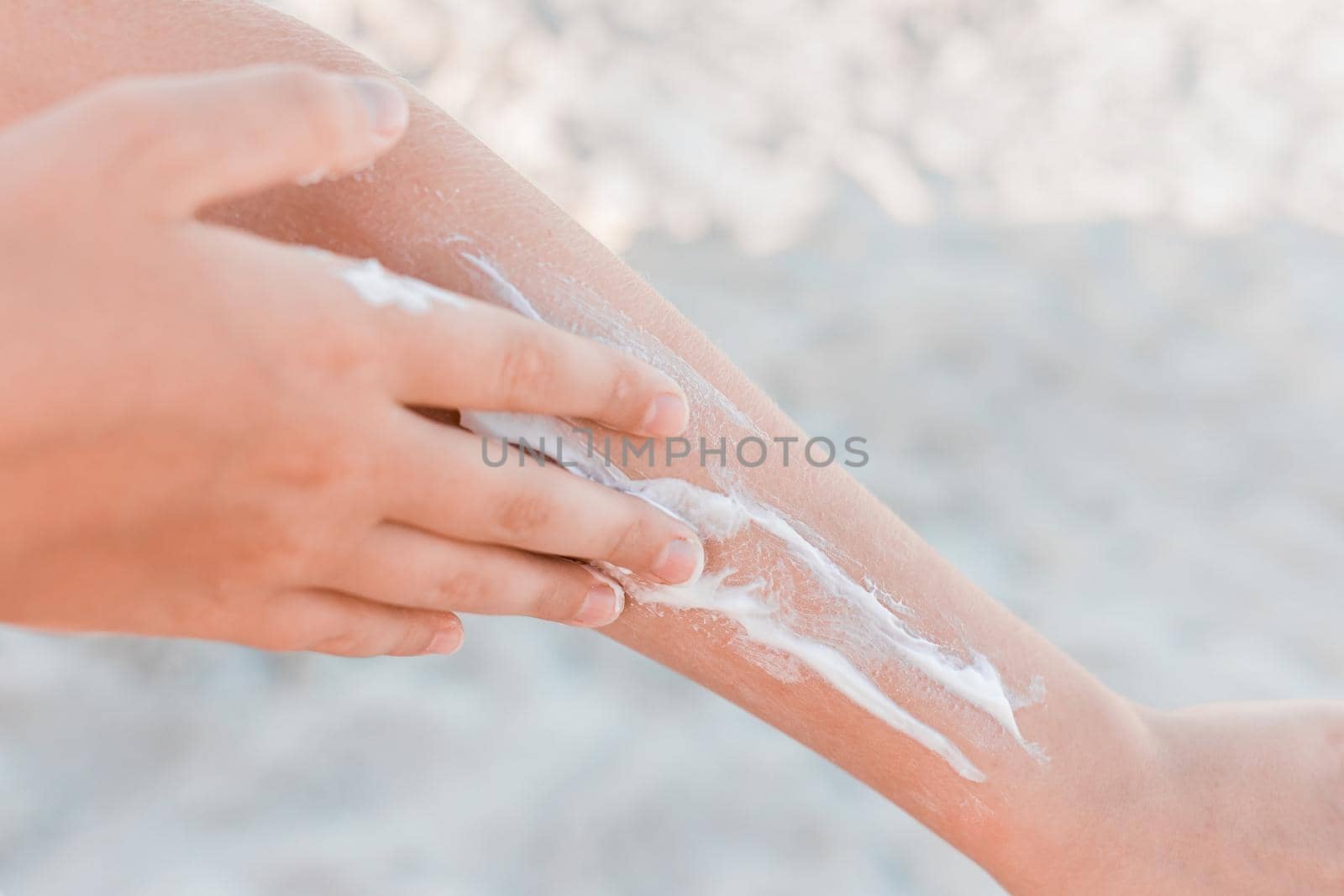 The hand of a young girl smears sunscreen and sun protection on the second hand against the background of the beach, close-up by AYDO8