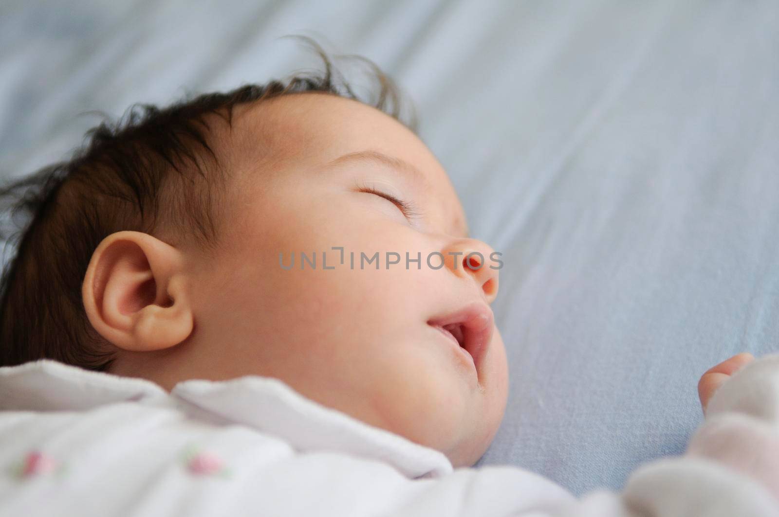 Newborn baby girl sleeping on blue sheets at home