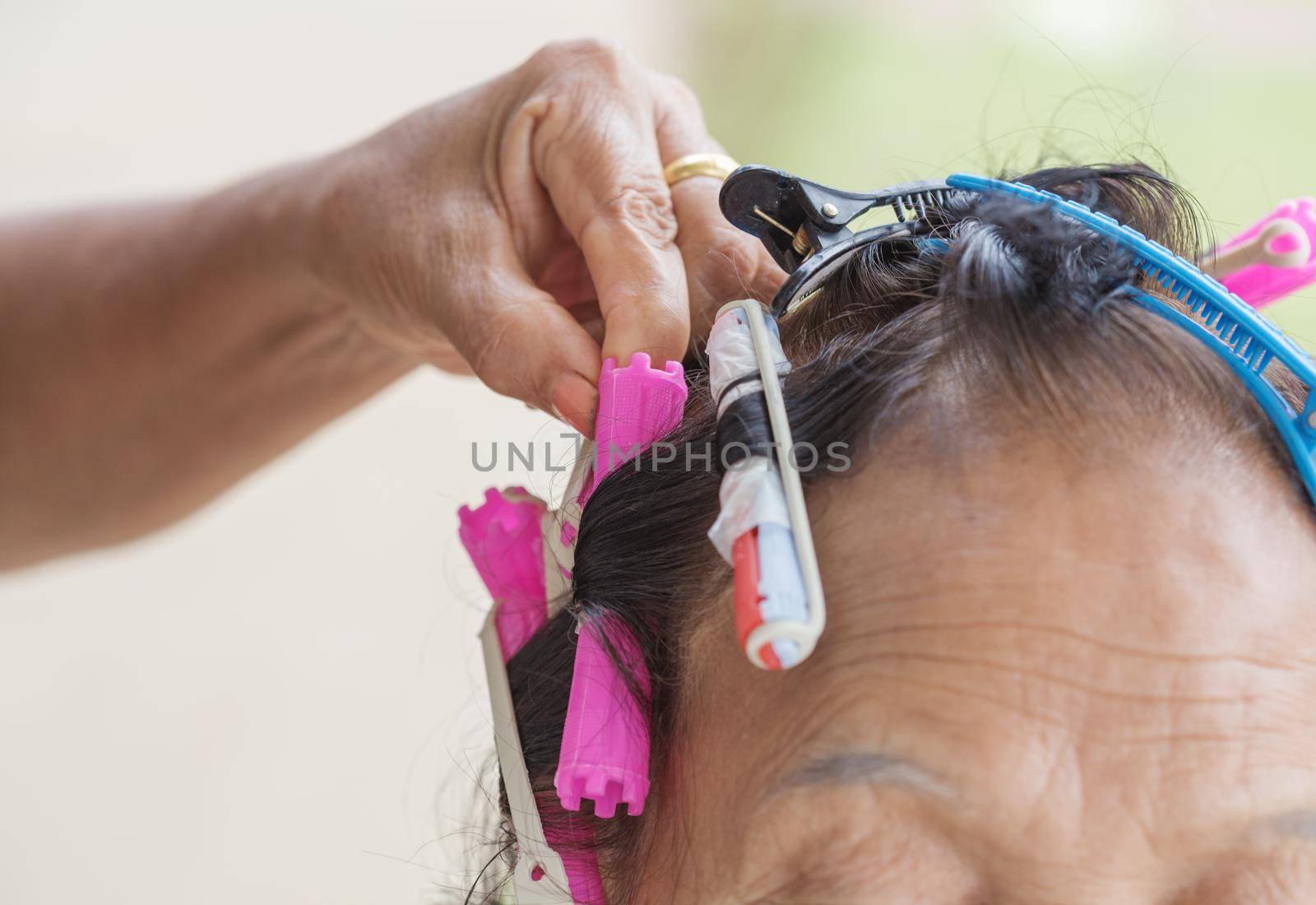 hand of a hairstylist doing a perm rolling hair of senior woman by geargodz