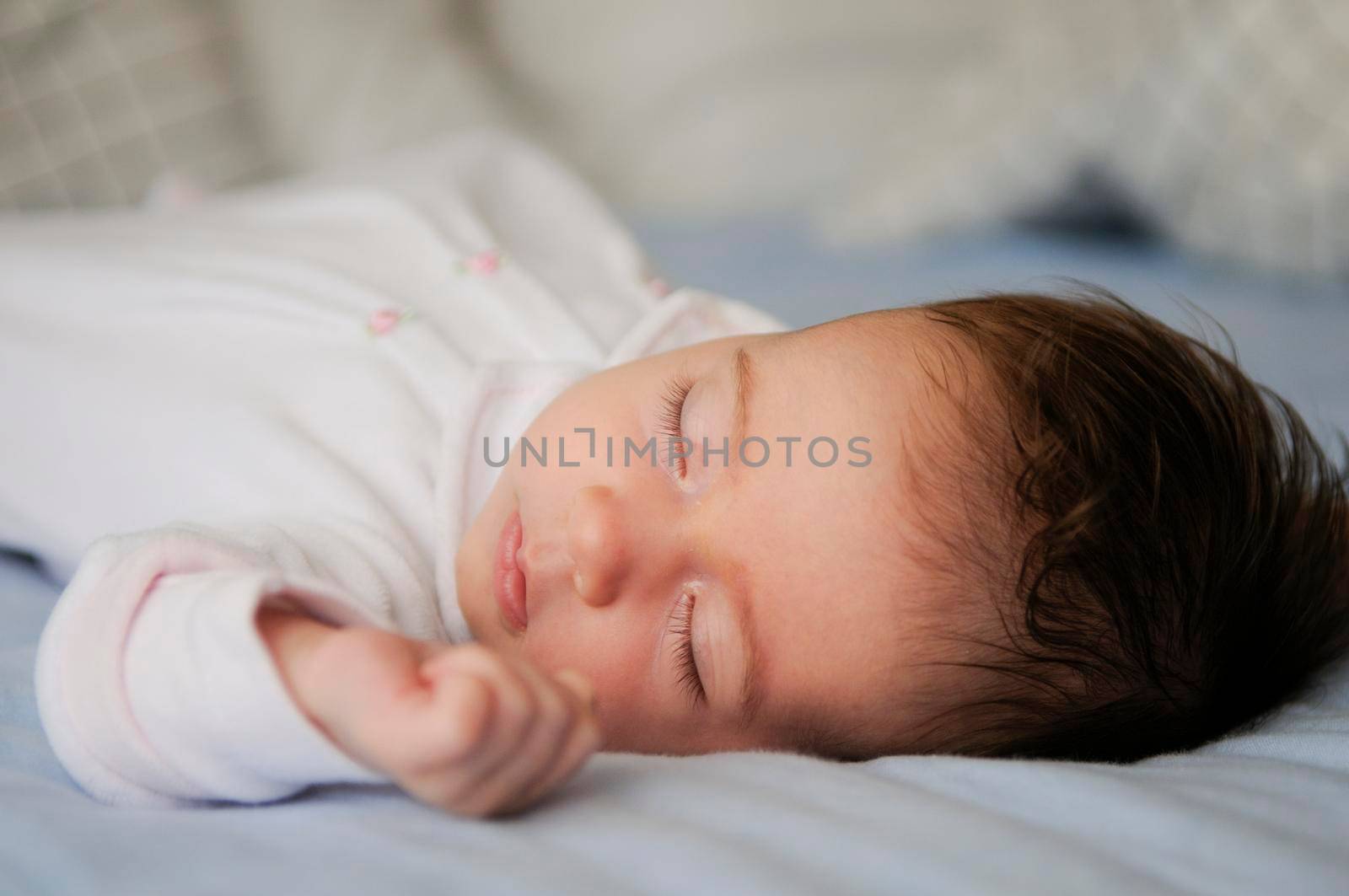 Newborn baby girl sleeping on blue sheets at home