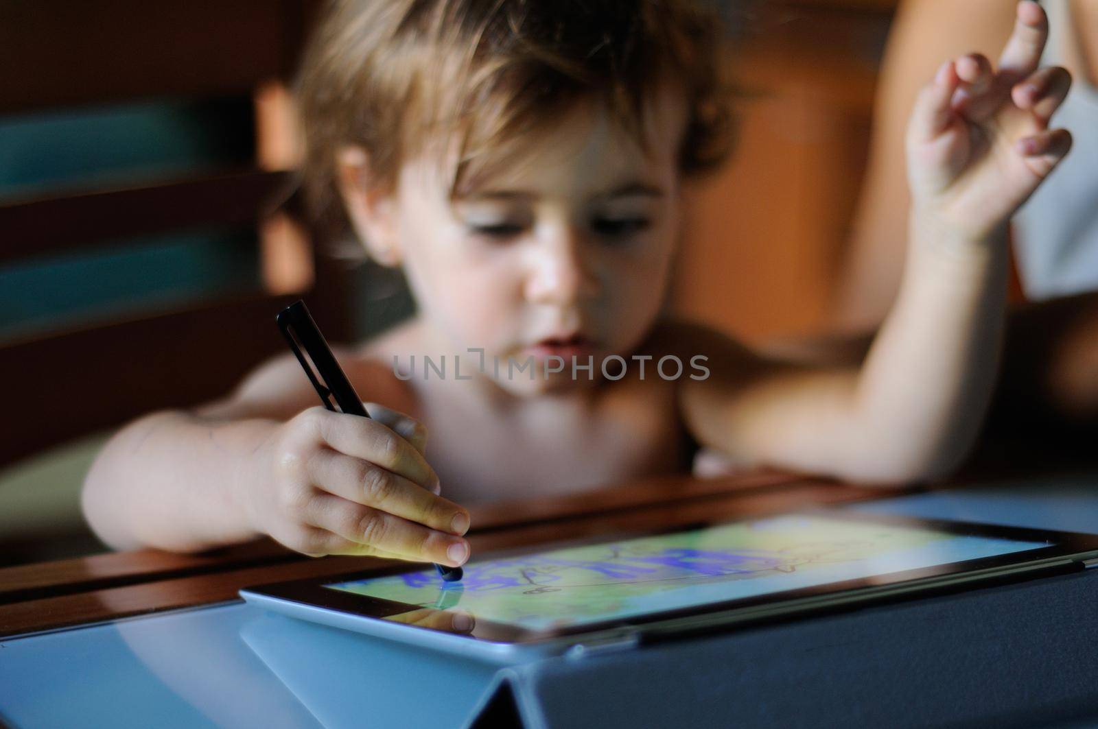 Little girl, two years old, painting with a digital tablet at home.