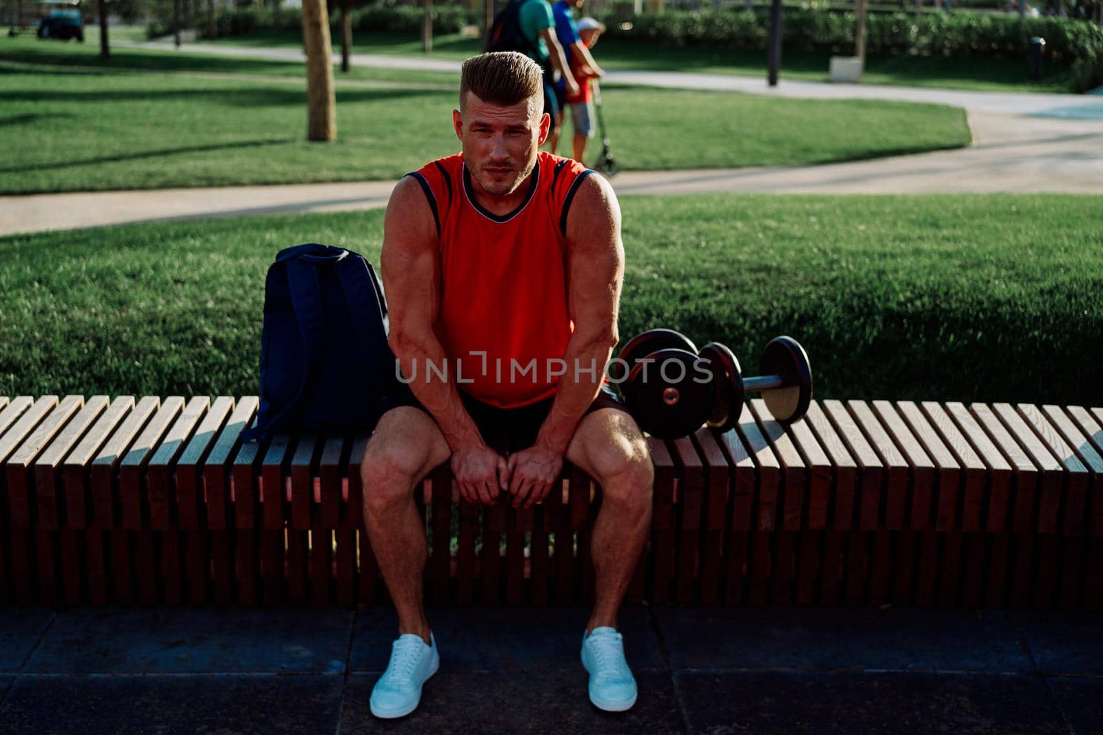 Cheerful male athlete in the park sits on a bench by Vichizh