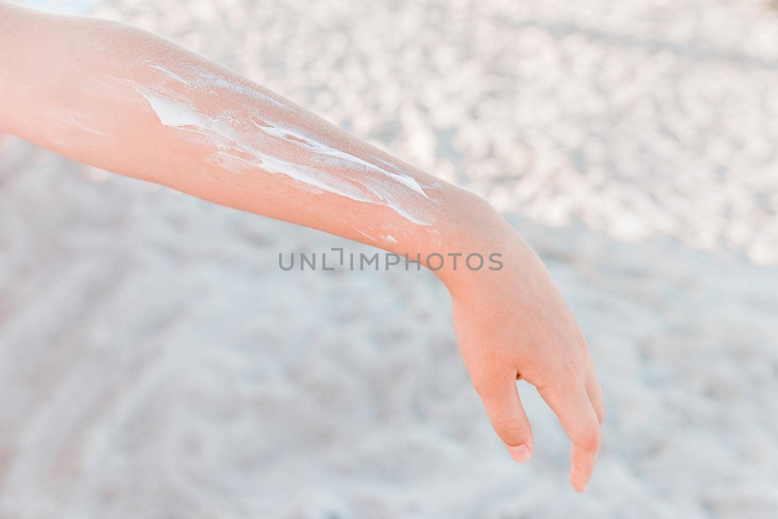 The hand of a young girl with a white pattern of sunscreen and protection from sunlight against the background of beach sand.