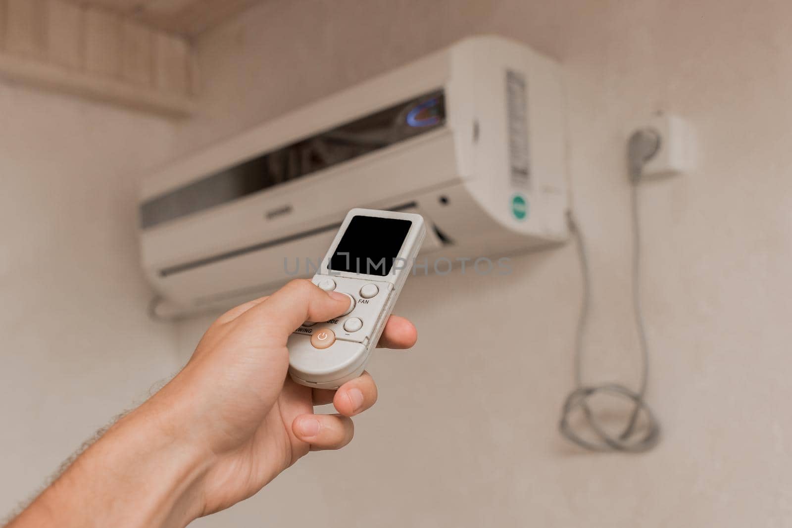 The guy's hand holds the remote control of the air conditioner. Cooling and temperature control in the room of the house.