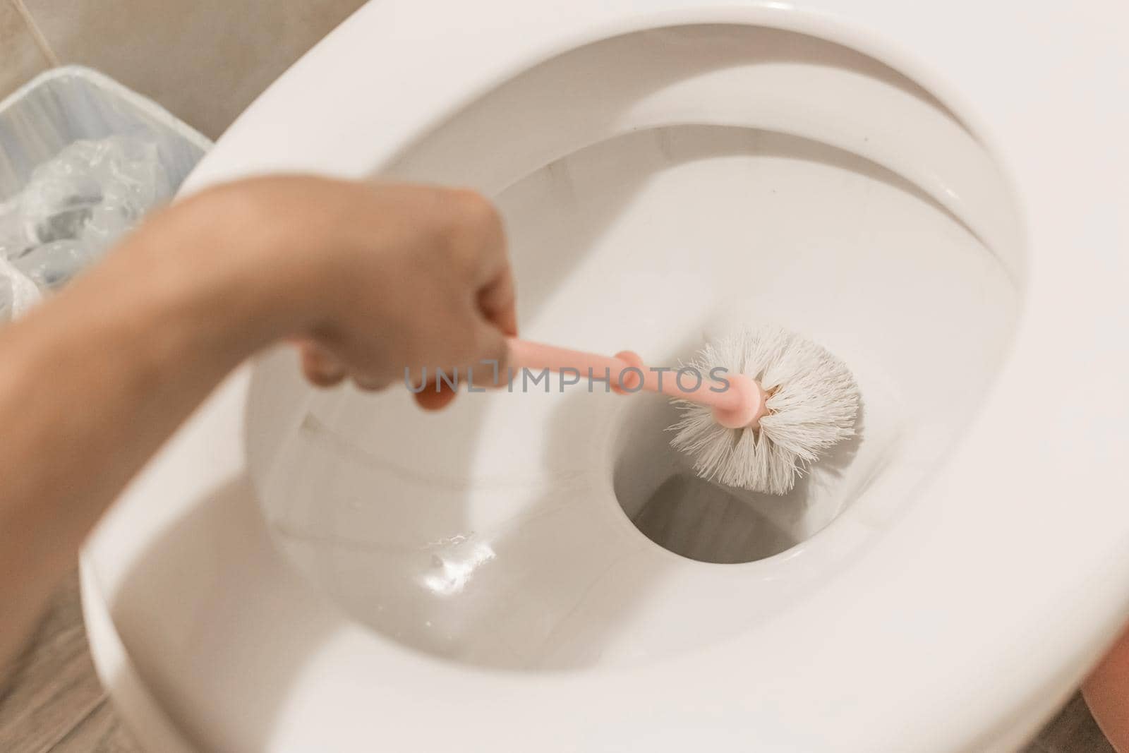 The guy's hand holds the toilet brush and cleans the toilet. The concept of home cleaning and hygiene in the bathroom.