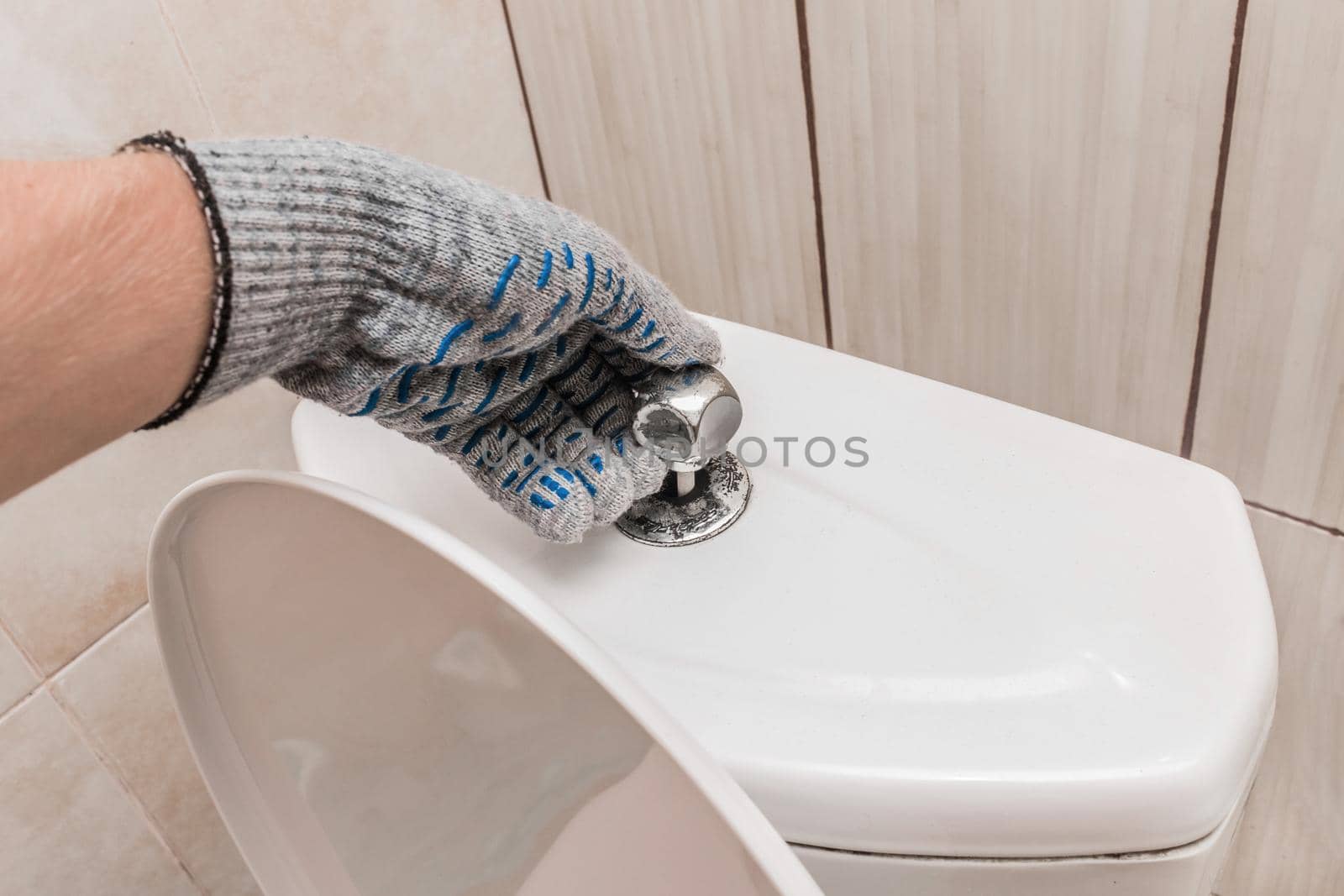 The hand of a plumber in a construction glove checks the serviceability of the toilet barrel. Professional repair of sanitary premises.