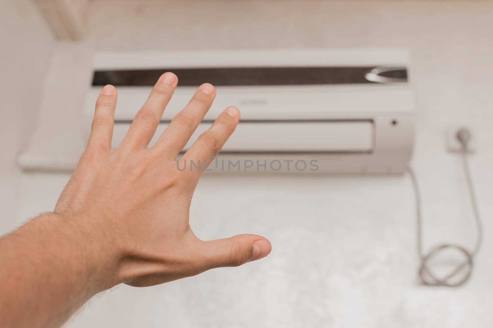 The guy puts his hand under the air conditioner in the room to check the temperature and the feeling of warm or cold air by AYDO8