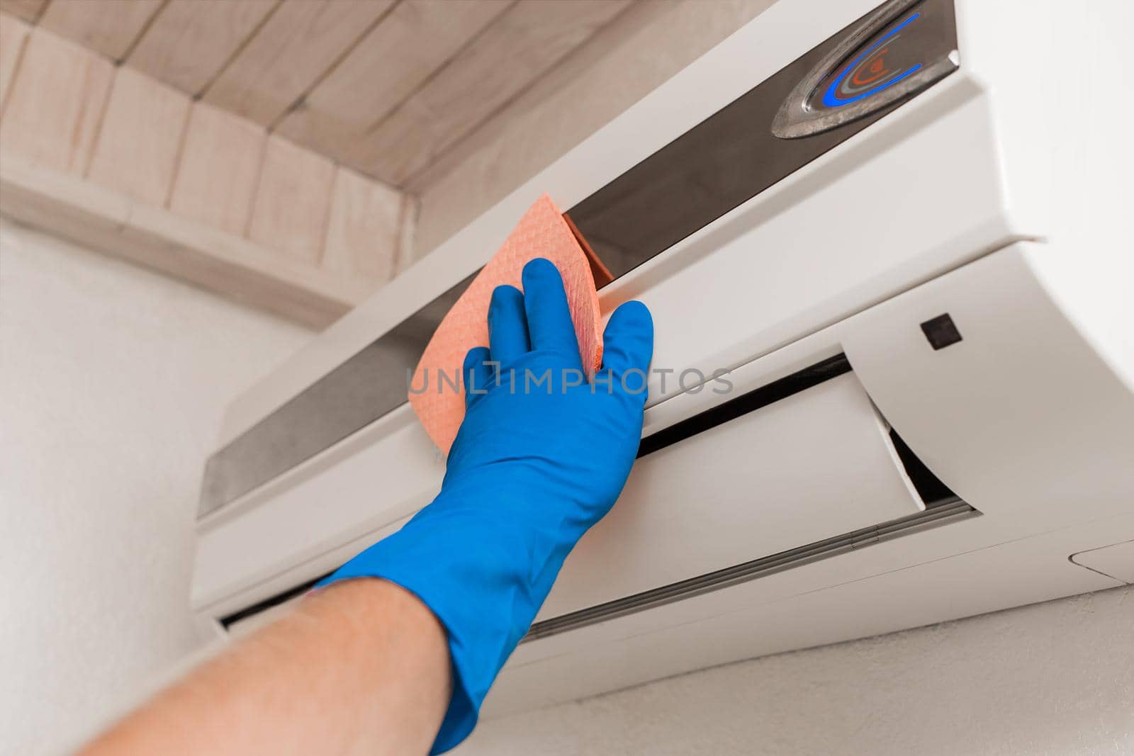 The hand of a man in a blue rubber household glove wipes and cleans the air conditioner. Maintenance and cleaning indoor service by AYDO8