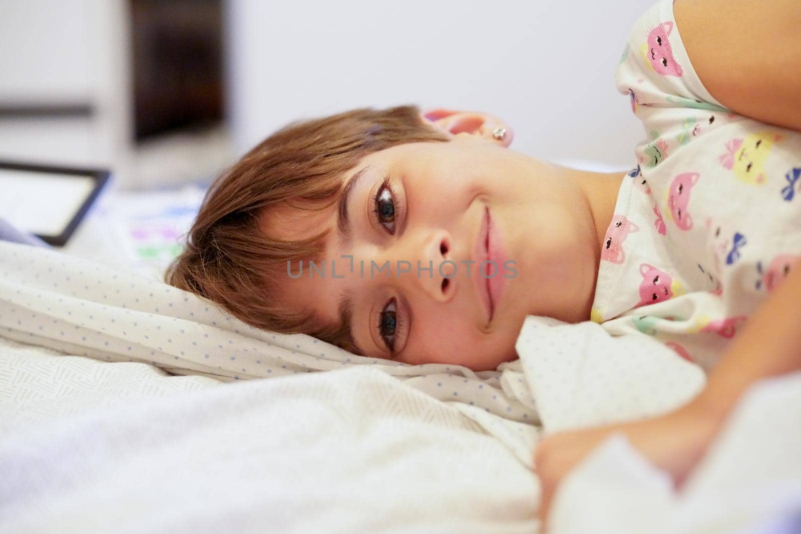 Happy little girl, eight years old, lying on her bed at home. smiling to camera.