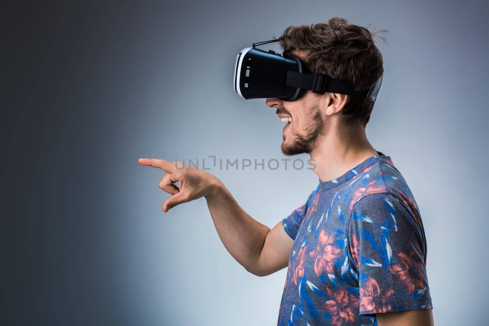 Side view of a young guy using a VR headset on a gray background. Studio shoot. Emotions