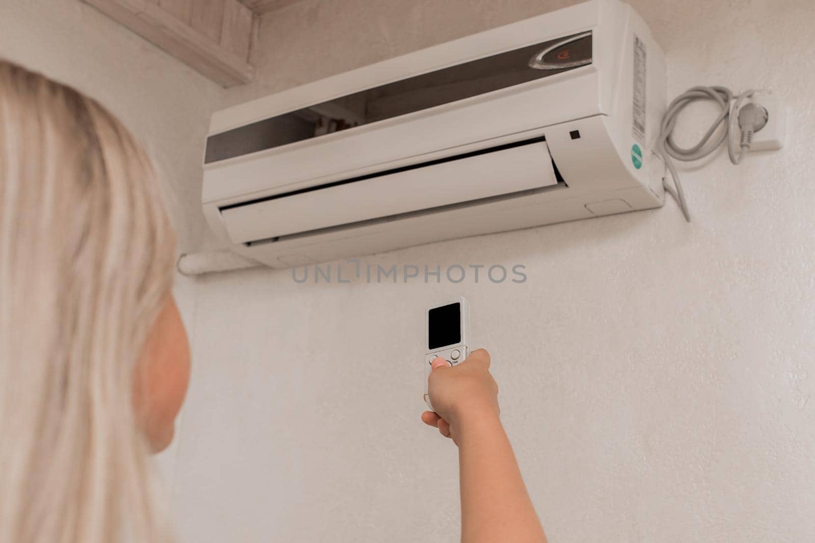 Young girl blonde teenager holds in his hands a remote control of air conditioning in the interior of the room.