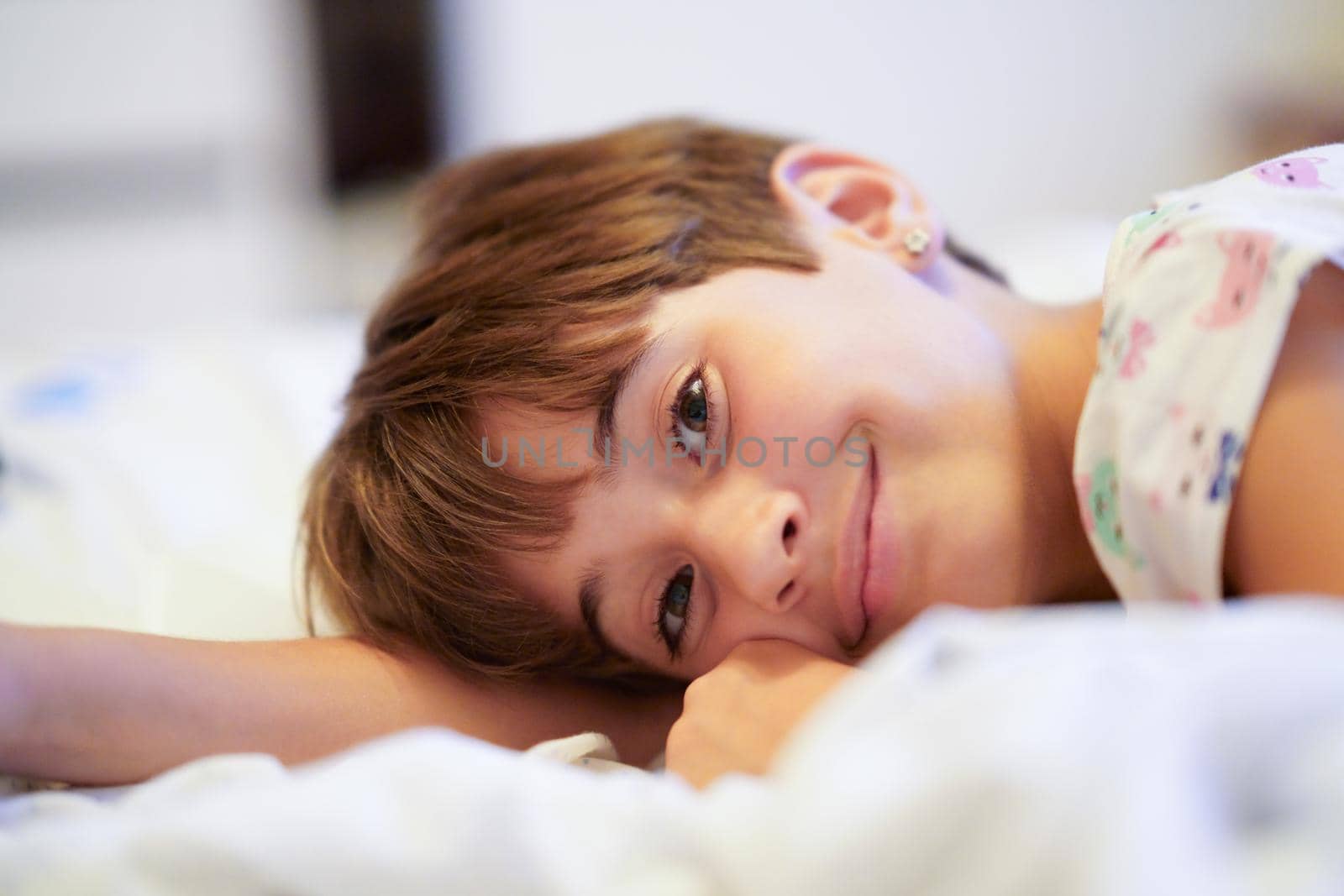 Happy little girl, eight years old, lying on her bed at home. smiling to camera.